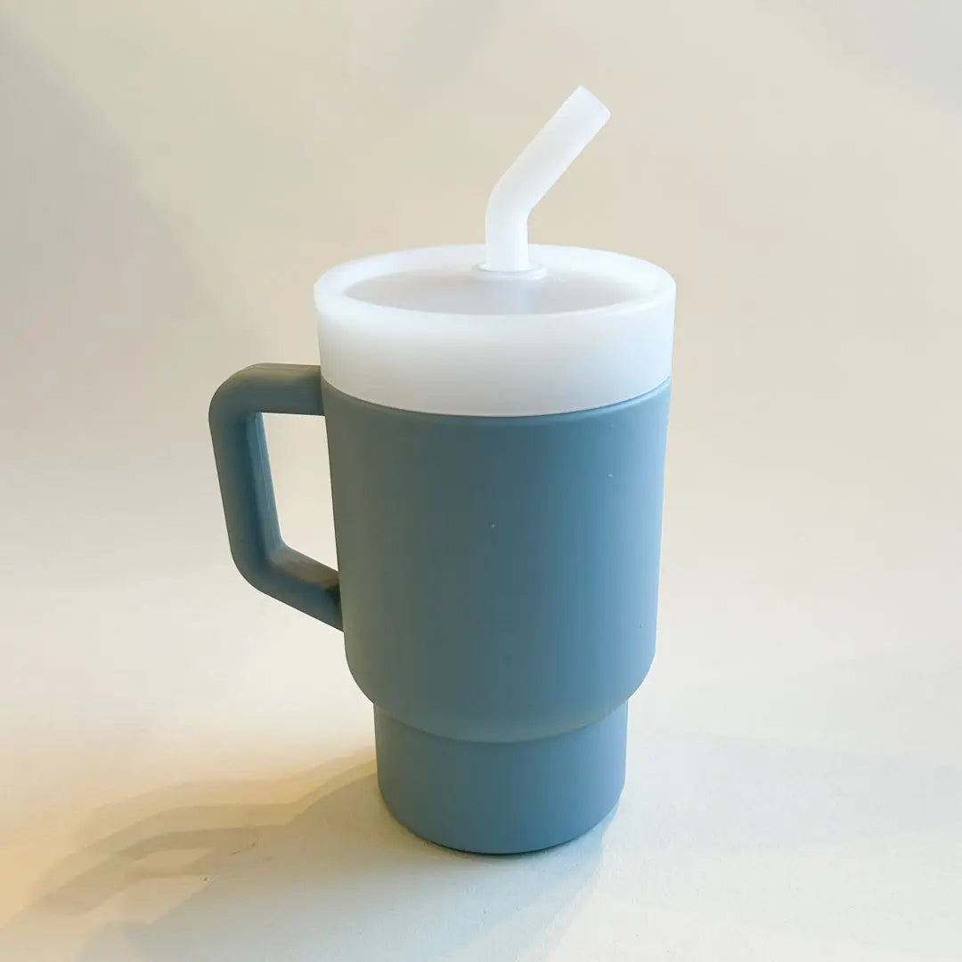 A lightweight 9oz toddler tumbler in soft, premium silicone, designed with a handle for easy grip and portability. The tumbler features a leak-resistant straw with a soft silicone tip, making it perfect for independent sipping. Available in playful colors for kids, it combines functionality with fun for little explorers. Denim blue, unisex color for boys and girls.