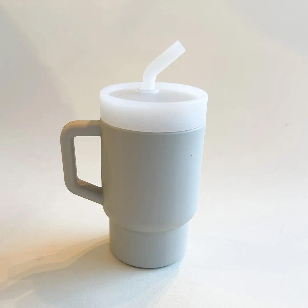 A lightweight 9oz toddler tumbler in soft, premium silicone, designed with a handle for easy grip and portability. The tumbler features a leak-resistant straw with a soft silicone tip, making it perfect for independent sipping. Available in playful colors for kids, it combines functionality with fun for little explorers. Light grey, unisex color for boys and girls.