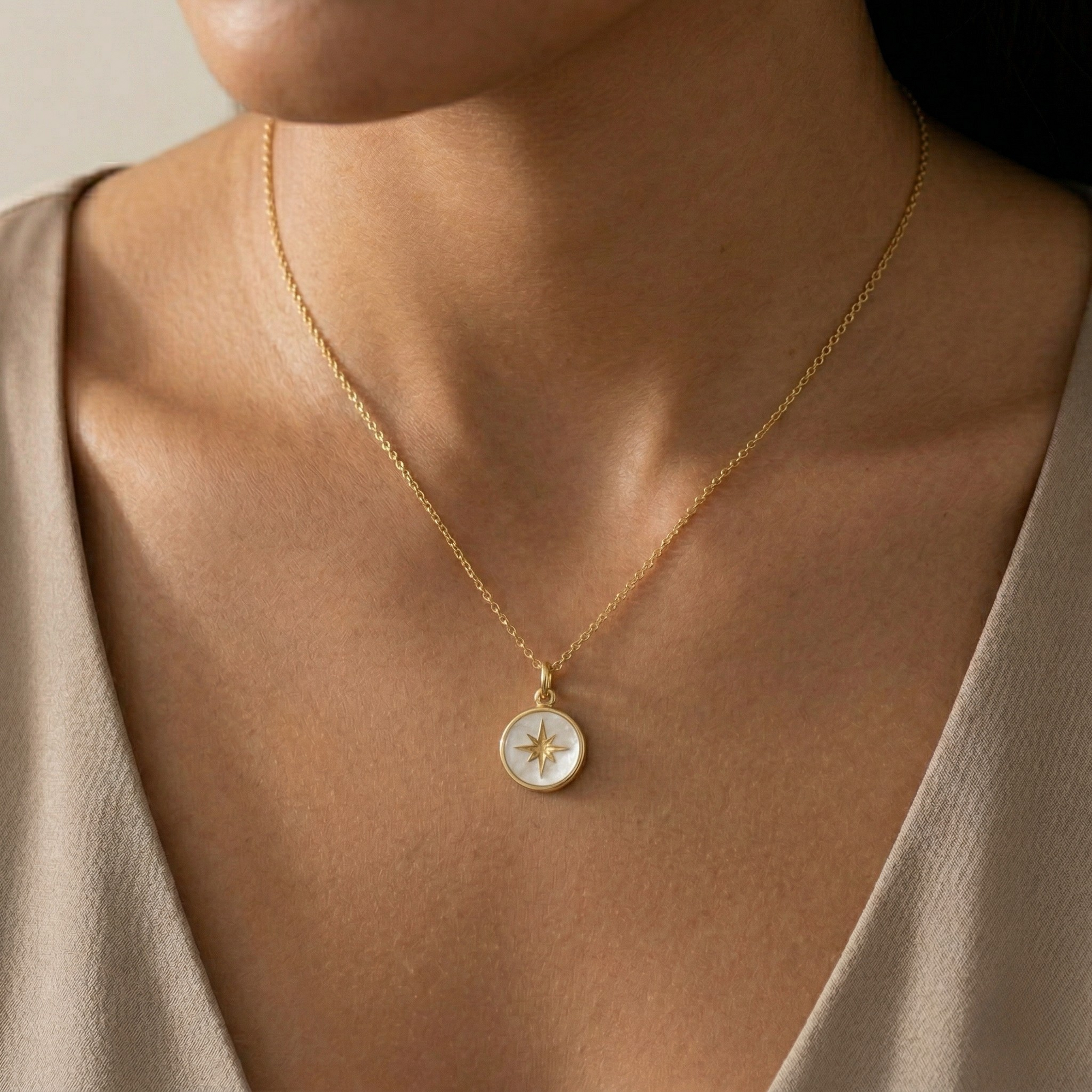 Close-up of Miminoo's Pearl Acrylic North Star Necklace featuring a round pearl marble acrylic charm with a hand-painted gold star, suspended from a delicate 18k gold-plated chain on a white background on a woman wearing a beige top