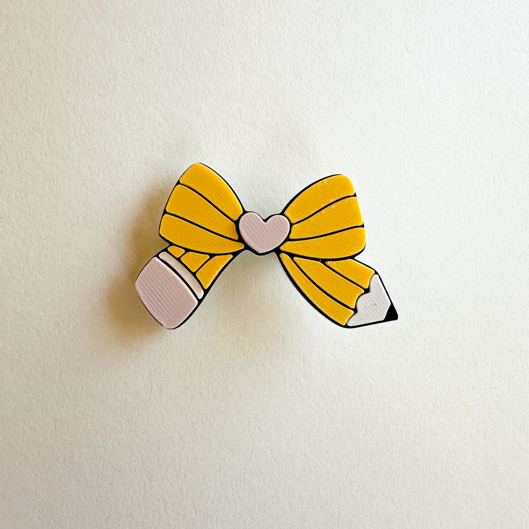 Hair clip with a design of a pencil with a yellow bow on a white background
