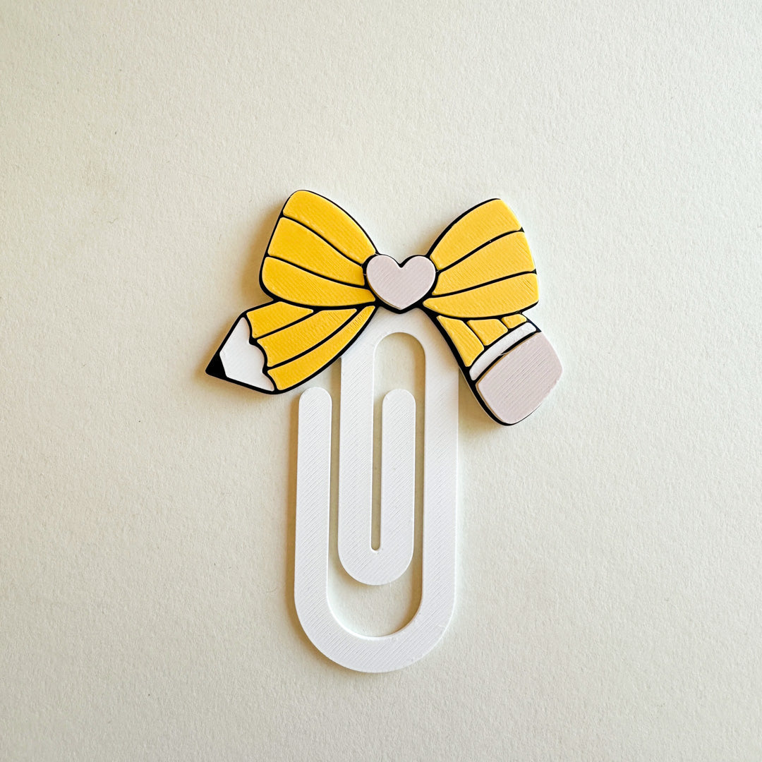 Pencil-shaped paper clip bookmark with yellow bow on a beige background