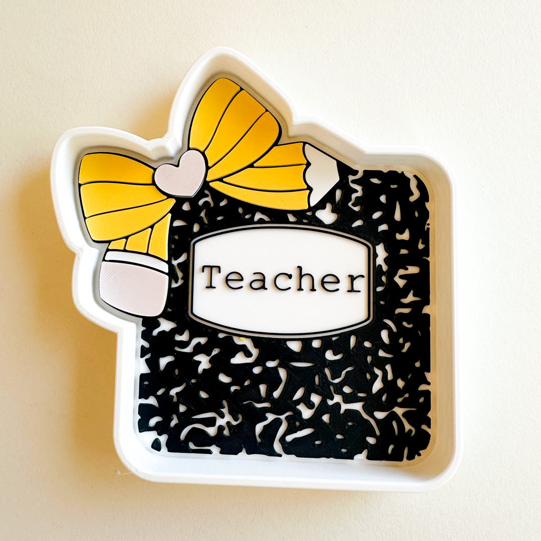 Decorative book-shaped trinkets dish with a yellow bow and 'Teacher' label on a beige background